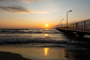 Fototapeta na wymiar Golden sunrise and foamy waves over pontoon bridge at Black Sea