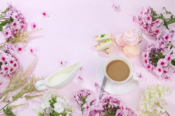 Colorful flowers of pink phlox, cup of coffee and marshmallow with pastilla on a wooden table, top view with place for text, flat lay-out, selective focus.