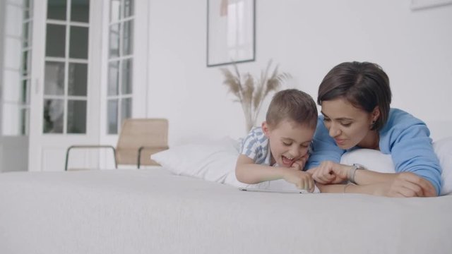 Happy young mother showing cartoon on digital tablet to her toddler son before going to sleep. Happy mother showing cartoon on digital tablet to her toddler son.