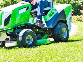 Senior man driving a tractor lawn mower in garden with flowers