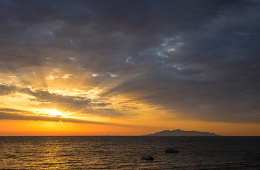 Sunrise from Aegean sea, magical sun rays shining though clouds, silhouette of volcanic island( Anafi, Greece, seen from  Santorini island) on the background. Fresh beginning start concept.