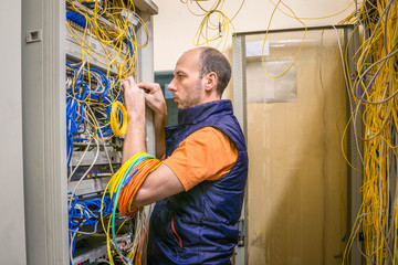System administrator commutes many messy wires in the server room. Technician works with data...