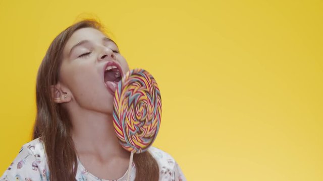 Happy child sucking lollipop on yellow background