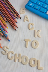 Top view of several diagonal colored pencils and blue calculator, with the words back to school, on white wooden background in vertical