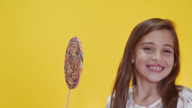 Happy child sucking lollipop on yellow background