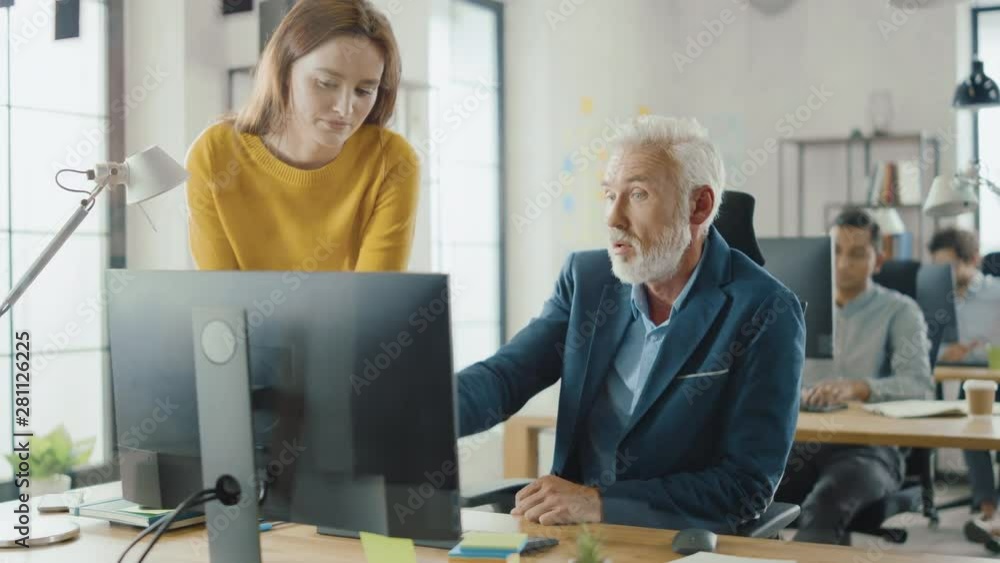 Poster Handsome Middle Aged Creative Engineer Sitting at the Desk working on Desktop Computer Has Discussion with Beautiful Female Project Manager. Office with Friendly Colleagues Chatting, Finding Solutions