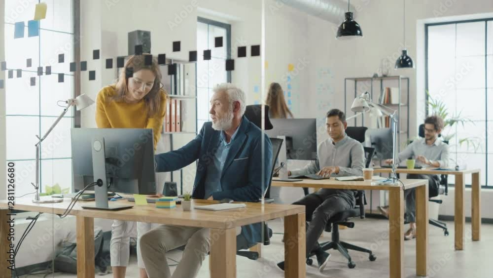 Poster Handsome Middle Aged Creative Engineer Sitting at the Desk working on Desktop Computer Has Discussion with Beautiful Female Project Manager. Office with Friendly Colleagues Chatting, Finding Solutions