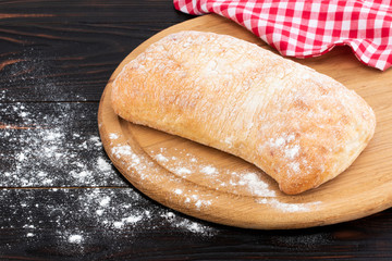 Loaf of ciabatta bread on a cutting board on the dark wooden table