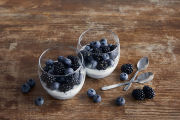 tasty breakfast with yogurt and berries in glasses near teaspoons on wooden table