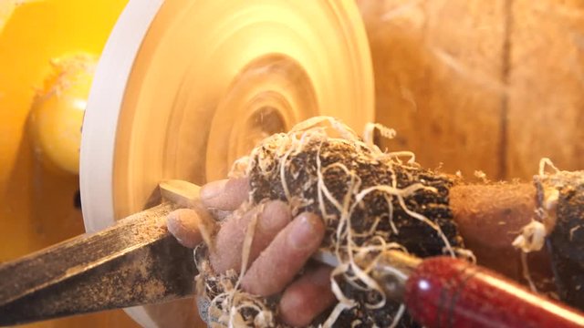 Carpenter handles wood by lathe. Builder works with workpiece in workshop. Making beautiful wooden handmade dish. Production of unusual plate. Woodworker cuts wood by chisel in soft focus.