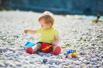 Adorable toddler girl playing with pebbles on the beach