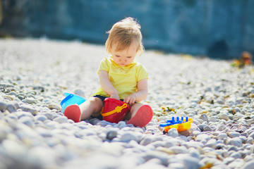 Adorable toddler girl playing with pebbles on the beach