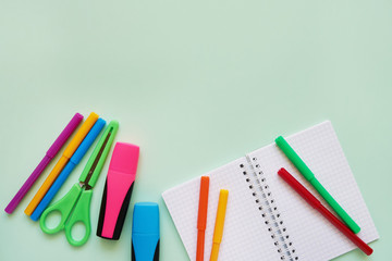 School subjects on a green background. Notepad, colored scissors and felt tip pens. Back to school concept. Flat lay, copy space