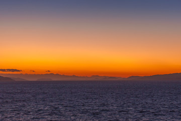 Dreamlike sunset with orange sky and islands of the Aegean Sea at horizon
