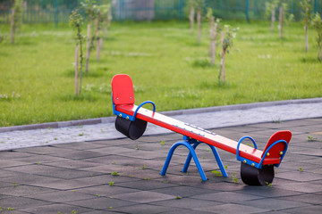 Seesaw swing in big yard with soft rubber flooring on sunny summer day.