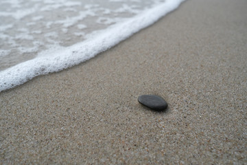 Fototapeta na wymiar Dark stone on the sand by the water
