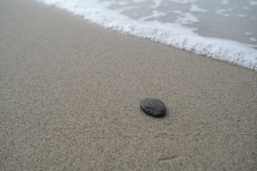 Fototapeta na wymiar Dark stone on the sand by the water
