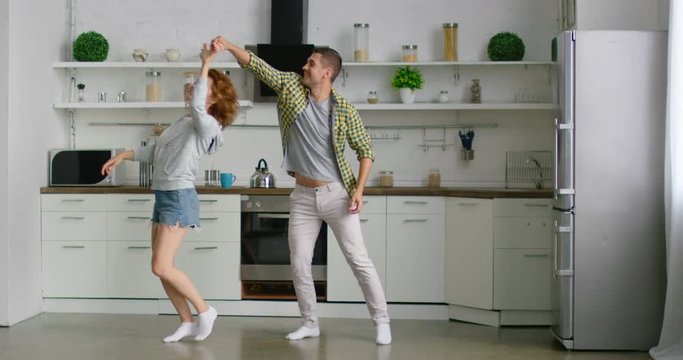 Happy young man and woman are dancing in the morning in kitchen, enjoying their relationships, jumping, laughing, celebrating their weekend together, being in love, interior. 4K, shot on RED camera