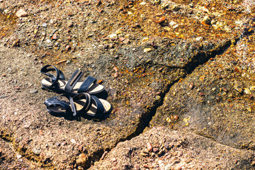 empty old female sandals lay on a stone beach waterfront background 
