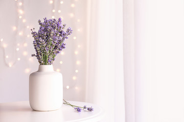 Beautiful lavender flowers in vase on table in room