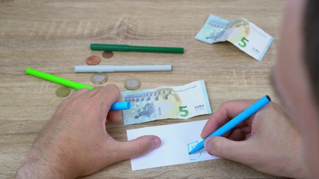 man draws a very bad copy of a bank note. funny video of making fake money. Counterfeiter forges banknotes. Fake concept. Fake money on a wooden background. Top view