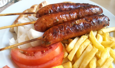 Grilled sausages on the stick with french fries and tomatoes