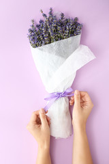 Female hands with bouquet of beautiful lavender flowers on color background
