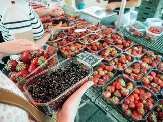 Closeup of woman hands holding shopping for fresh currant and strawberries on local farmers market - organic bio food harvested in French villages