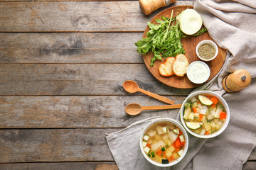 Bowls of tasty soup with bread, spices and sauce on wooden table