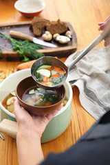 Woman pouring tasty soup from pot into bowl at table