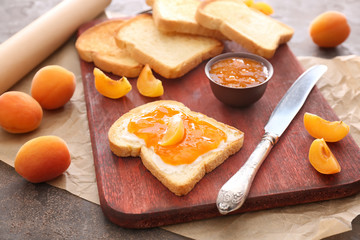 Bowl of tasty apricot jam and bread slices on board