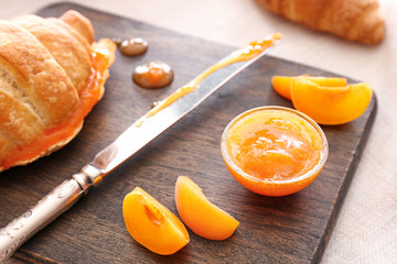 Tasty apricot jam with croissant on wooden board, closeup
