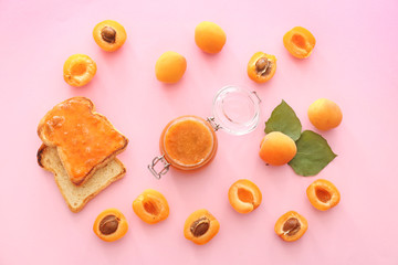 Tasty apricot jam with bread slices on color background