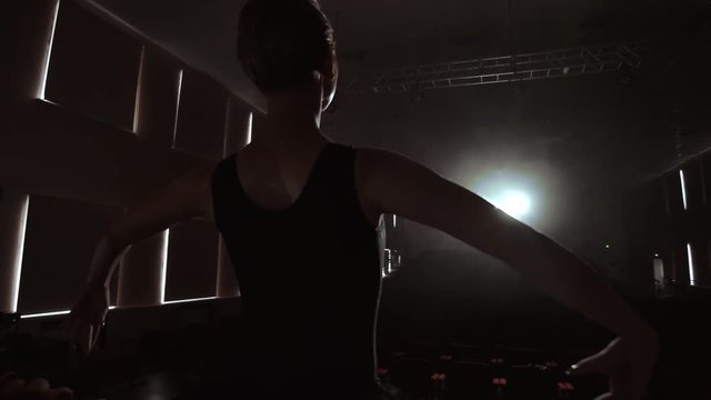 SLOW MOTION: prima ballet rehearses a solo performance standing on the stage of the theater in smoke in a black dress in the light