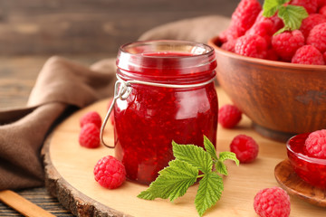Jar of tasty raspberry jam on wooden board