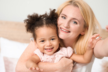 Happy woman with her little African-American daughter taking selfie at home