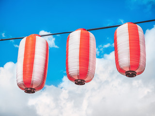 Paper red-white japanese lanterns Chochin hanging on blue sky background. Summer background