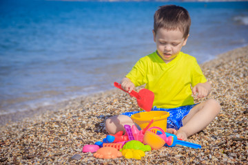 The boy plays on the beach in the toys for the sand. Children's games. Games on the beach. Galichny beach. Children's toys for sand. The baby is playing
