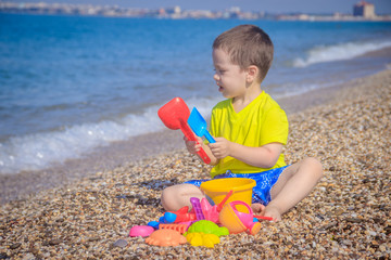 The boy plays on the beach in the toys for the sand. Children's games. Games on the beach. Galichny beach. Children's toys for sand. The baby is playing