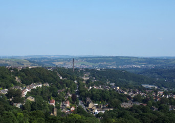 a panoramic view of the town of west yorkshire from above with streets and houses surrounded by trees and fields and the historic wainhouse tower on a hillside