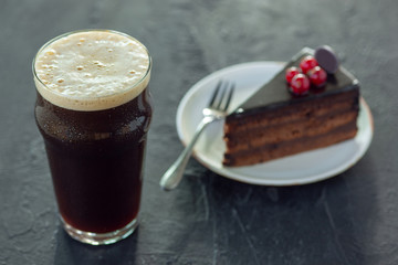 Glass of dark beer on the stone table background. Cold drink and truffles with cake are prepared for a big friend's party. Concept of drinks, fun, food, celebrating, meeting, oktoberfest.