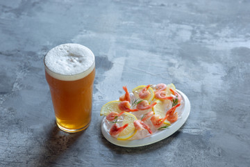 Glass of light beer on white stone background. Cold alcohol drink and shrimp with lemon are prepared for a friend's party. Concept of drinks, fun, food, celebrating, meeting, oktoberfest.