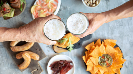Top view of two hands with beer glasses and delicious snacks. Sausages and sauces, chips, meat, shrimp with lemon. Concept of drinks, fun, food, celebrating, meeting, oktoberfest.