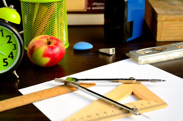 A4 sheet of paper, compasses, wooden square, wooden ruler, apple, pencil sharpener, eraser, wooden school pencil case on the desk.