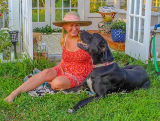 Happy and Casual Mature Woman 50-59 years old hanging out with her Great Dane in her garden in front of her beautiful greenhouse