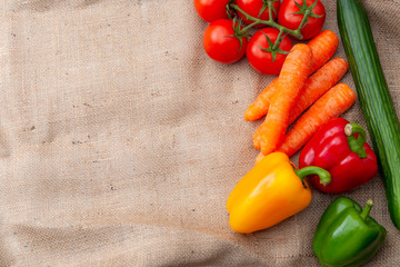 Fresh vegetables, vegetarian diet and vegan food concept theme with a group of tomatoes, peppers, carrots and cucumber isolated on a rustic burlap bag with copy space