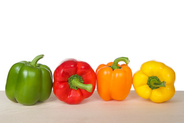 Bell Peppers on a wood table isolated on white. Green, red, orange and yellow varieties. Like the tomato, bell peppers are botanical fruits but culinary vegetables.