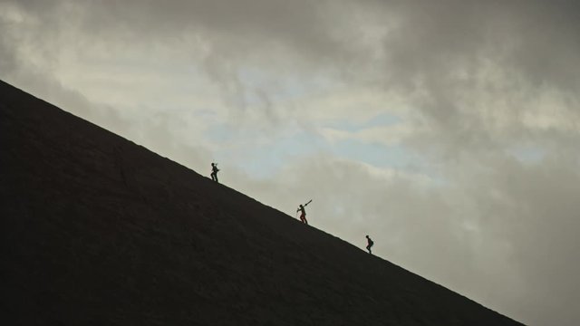3 silhouette friends trek up volcano side