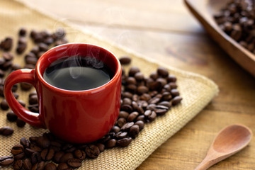 red cup of hot coffee, wooden spoon and coffee beans on wooden table
