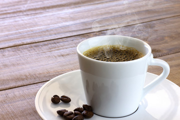 White cup of hot coffee with smoke on wood table with coffee beans